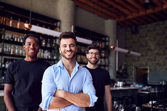 portrait of male owner of restaurant bar with team of waiting staff standing by counter